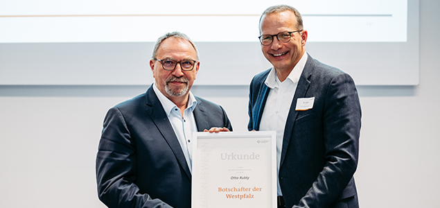 Zwei Männer blicken lächelnd in die Kamera und halten eine Urkunde mit dem Schriftzug "Botschafter der Westpfalz"